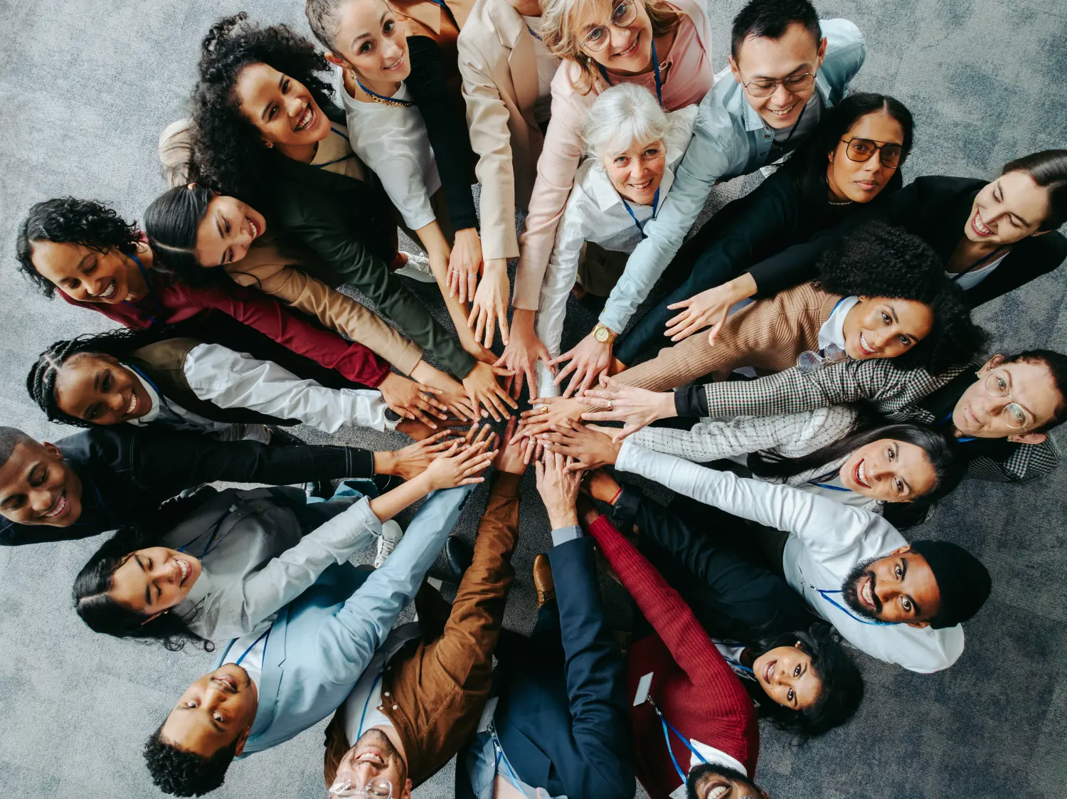 Linguana die Sprachschule - Verschiedene Teammitglieder mit den Händen in der Mitte, die in einer Geschäftsumgebung in die Kamera schauen 